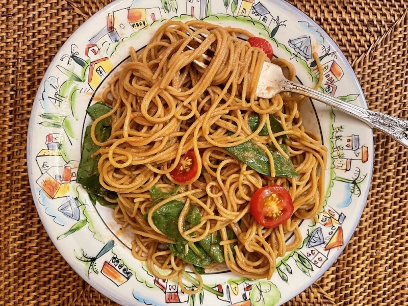 Oil free pasta with sauce, tomatoes, spinach and a fork on a colorful plate.