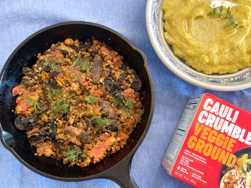 plantbased paprikash in a skillet with a bowl of polenta and a box of Big Mountain Food cauli crumbles