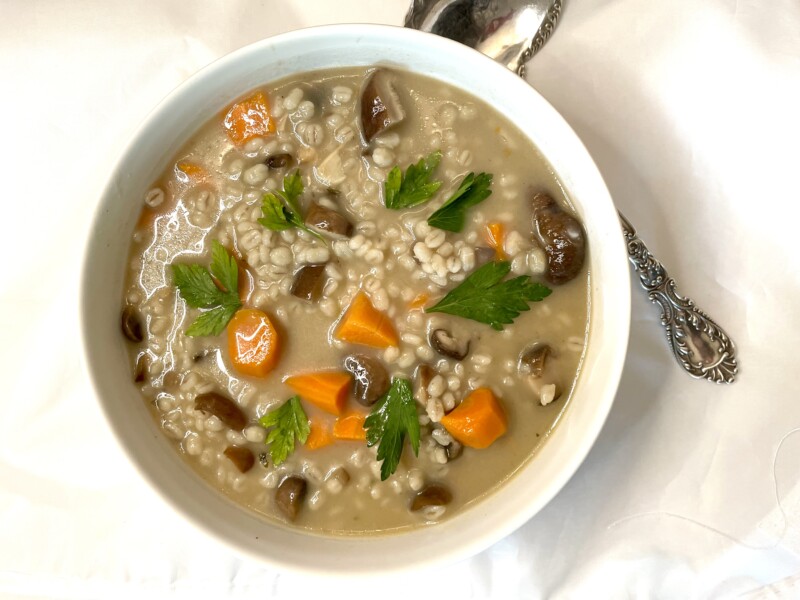 A white bowl of mushroom barley soup with a spoon.