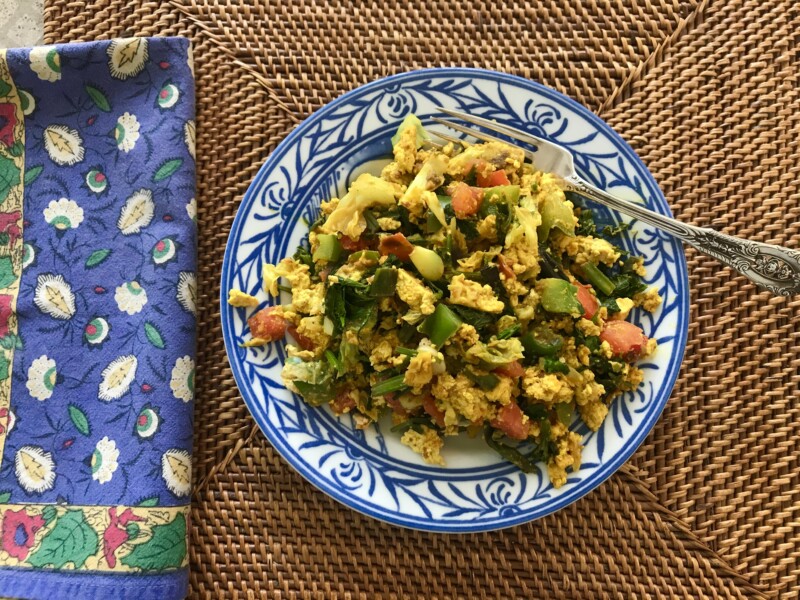 A plate of tofu scramble with vegetables and a fork. 
